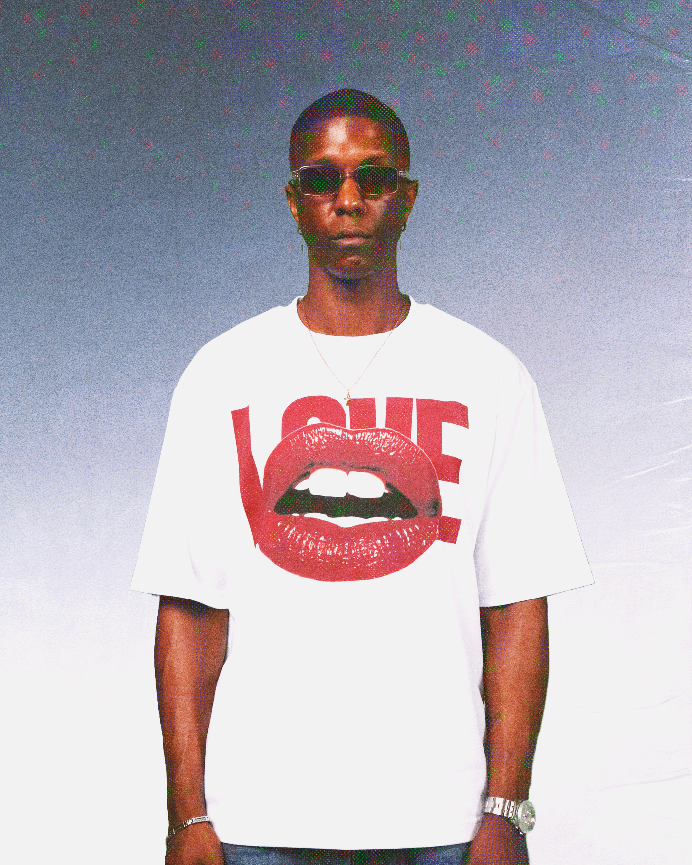 A fashion-forward black man wearing sunglasses and a bright red graphic T-shirt adorned with red lips, sporting a trendy summer streetwear style and exuding a vacation vibe.