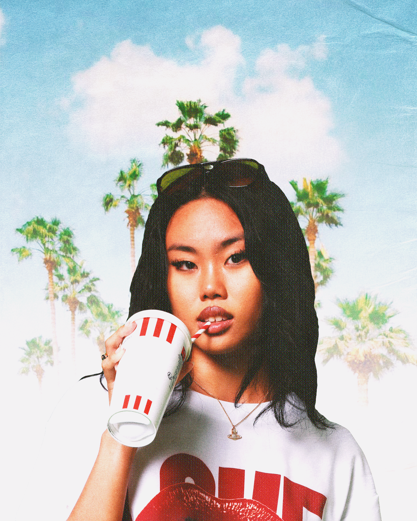 A fashion-forward woman asian wearing a white goblet with oversized red and white stripes and a bright red graphic T-shirt with red lips, posing in front of tropical palm trees and a blue sky  — a trendy summer streetwear style and vacation vibe.