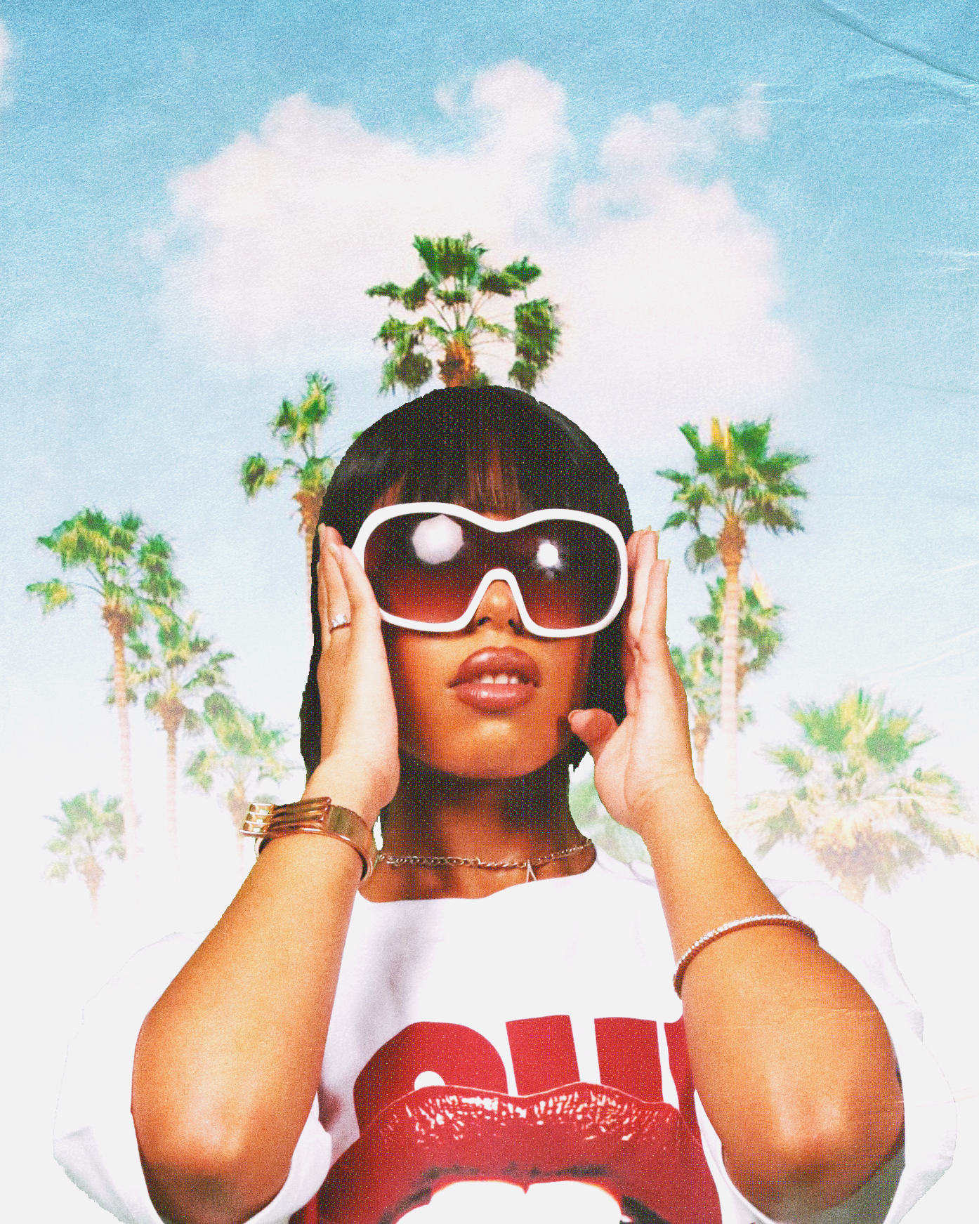 Fashion-forward woman wearing oversized white sunglasses and a bold red lips graphic t-shirt, posing in front of tropical palm trees and blue sky — trendy summer streetwear and vacation style.